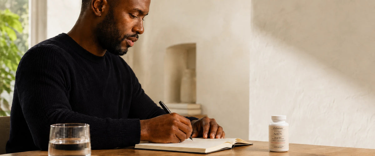 Man writing in a journal with Elaborate Energy NAD+ on the table
